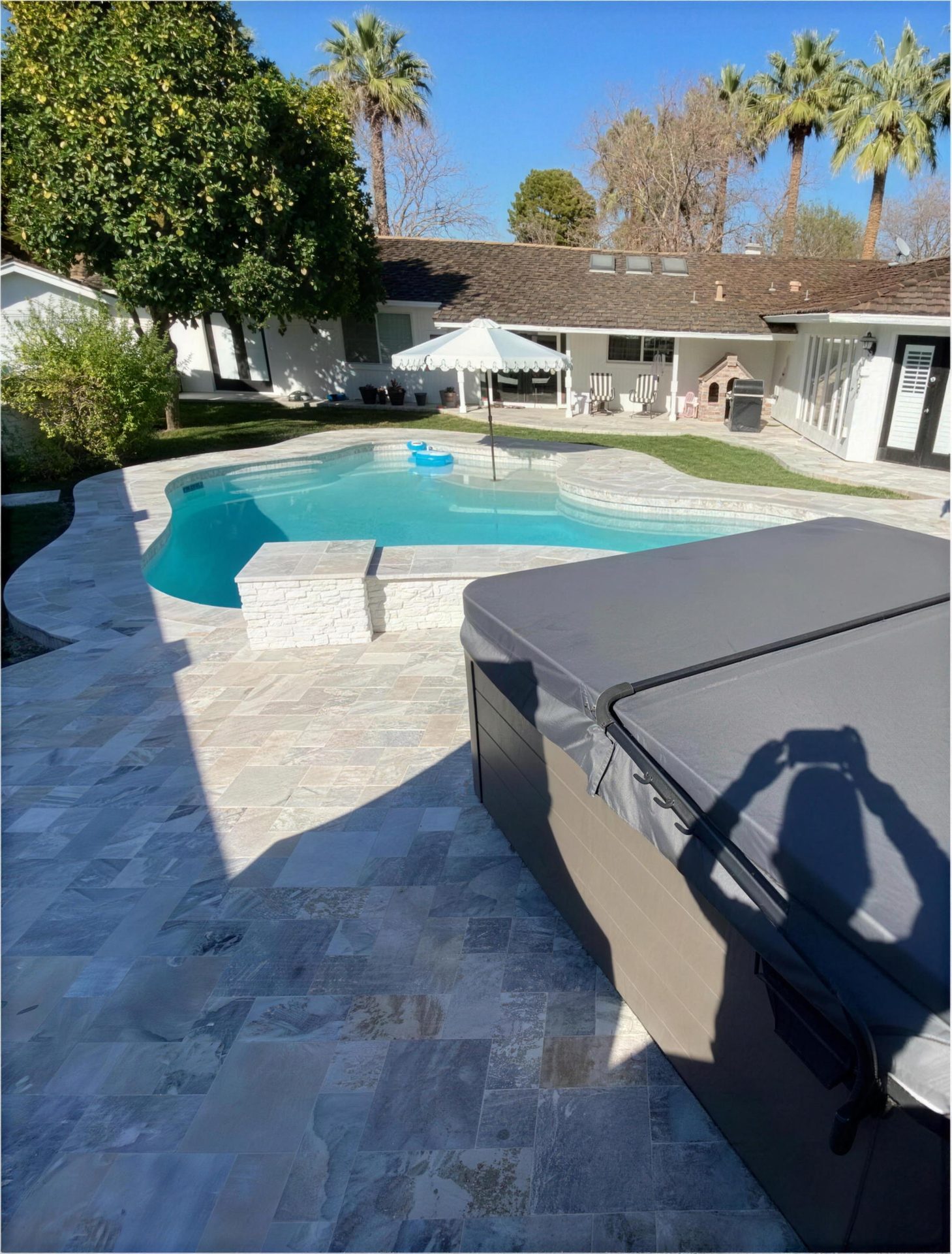 After: silver travertine deck, stacked-stone spa wall, and hot tub