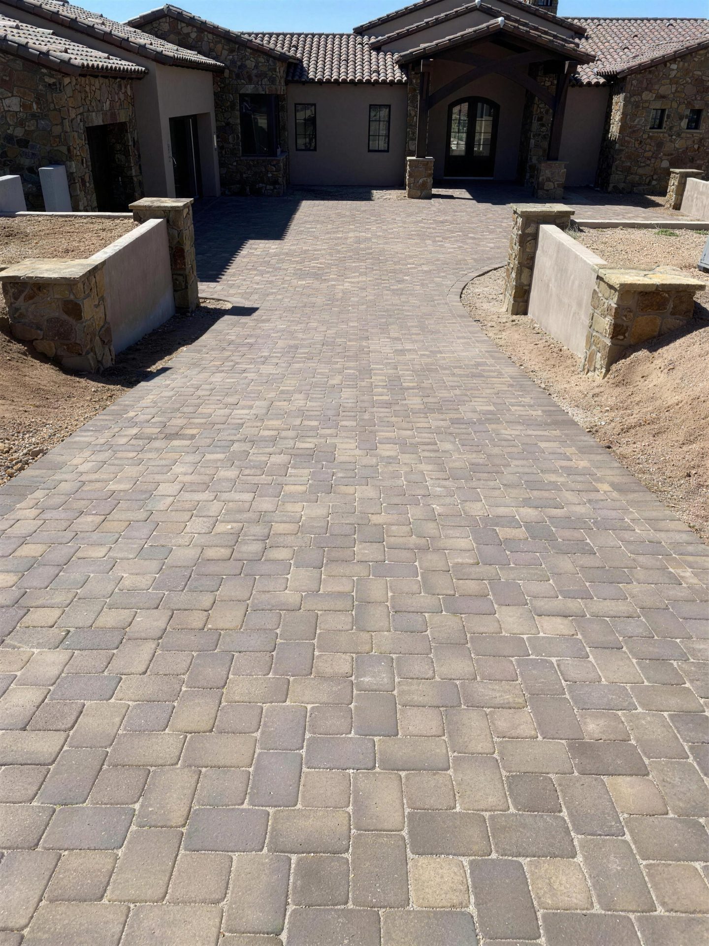 Cobble paver driveway leading to a stone-clad custom home