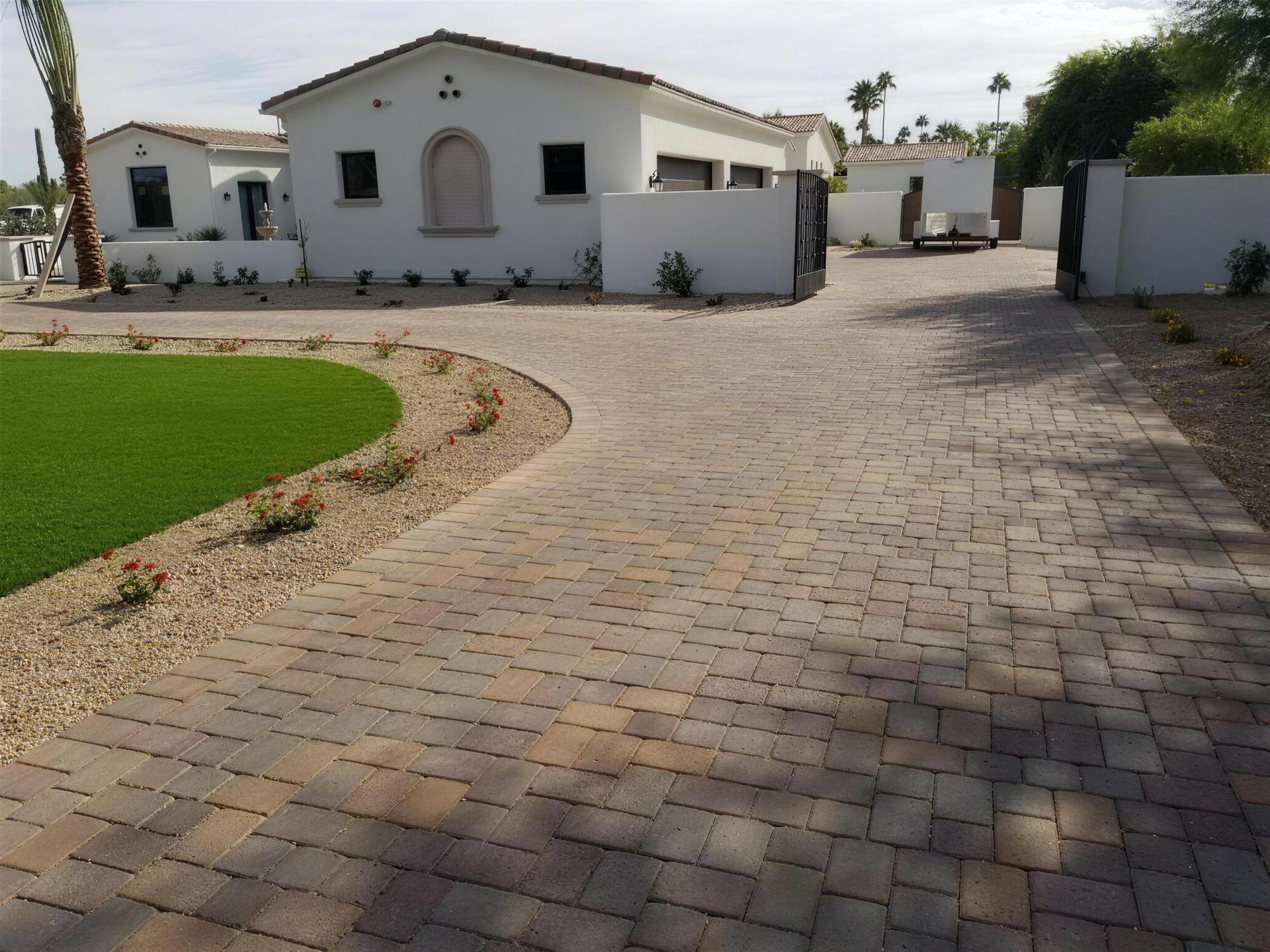 Cobblestone paver driveway wrapping an artificial turf lawn with a rose border