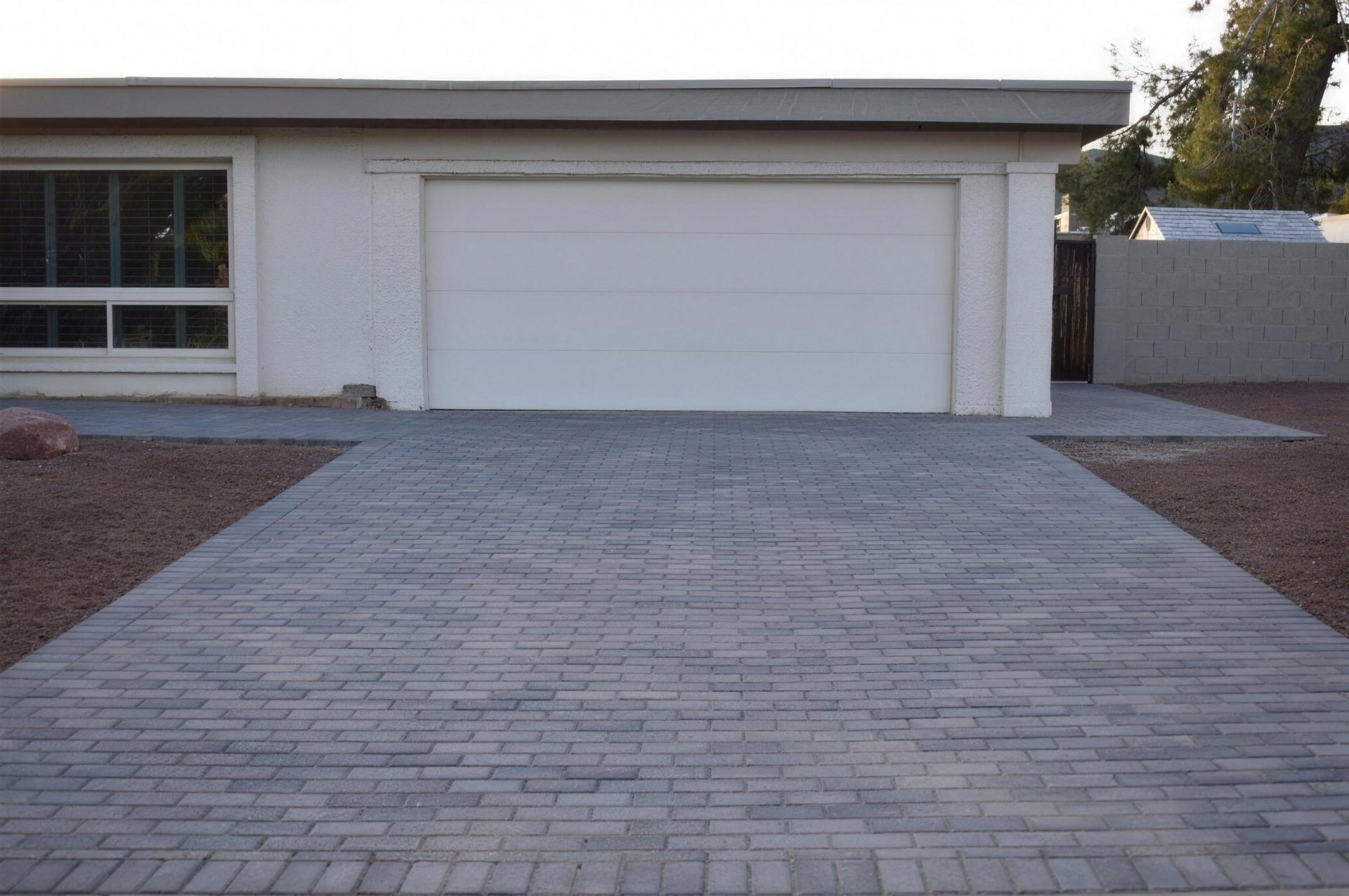 After: the same driveway rebuilt in gray interlocking pavers, widened to the gate