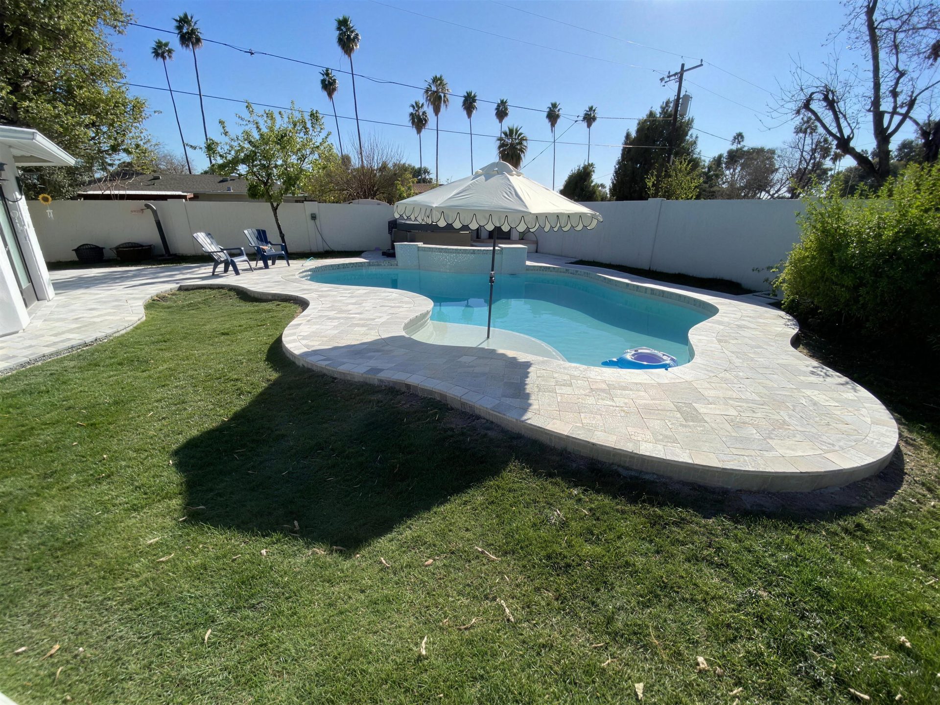 Travertine deck wrapping a backyard pool with a tanning-shelf umbrella